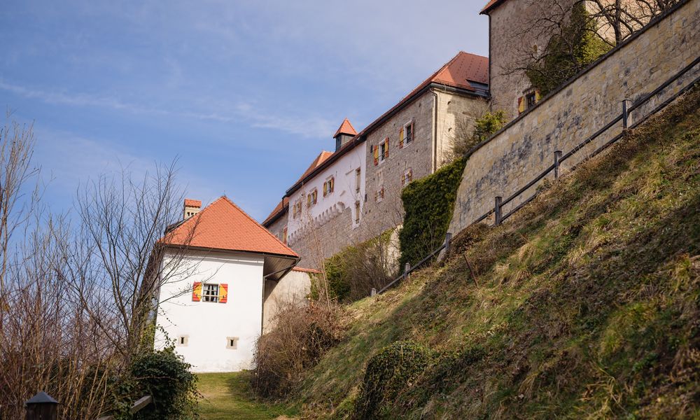 Pogled na grad Podsreda s travnate poti pod gradom, travnata pot vodi do mogočnega gradu iz svetlega kamna, rumeno-rdečimi polknami in rdečo streho.