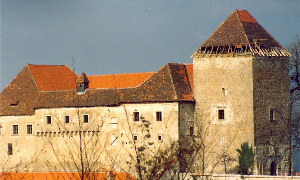 Pogled na grad Podsreda pred prenovo, večji del opeke je še rjave barve, del strehe ima že novo, rdečo kritino. Na stolpu je vidno ostrešje med prenovo.