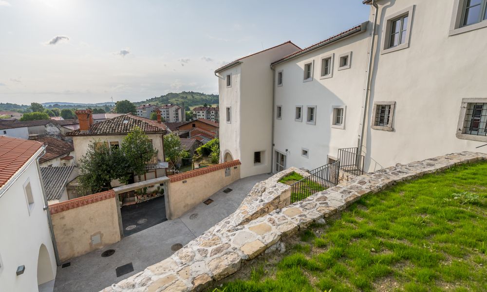 Zunanja podoba Muzeja prevozništva in tovorništva slikana iz travnatega dvorišča, v ozadju pogled na Senožeče.