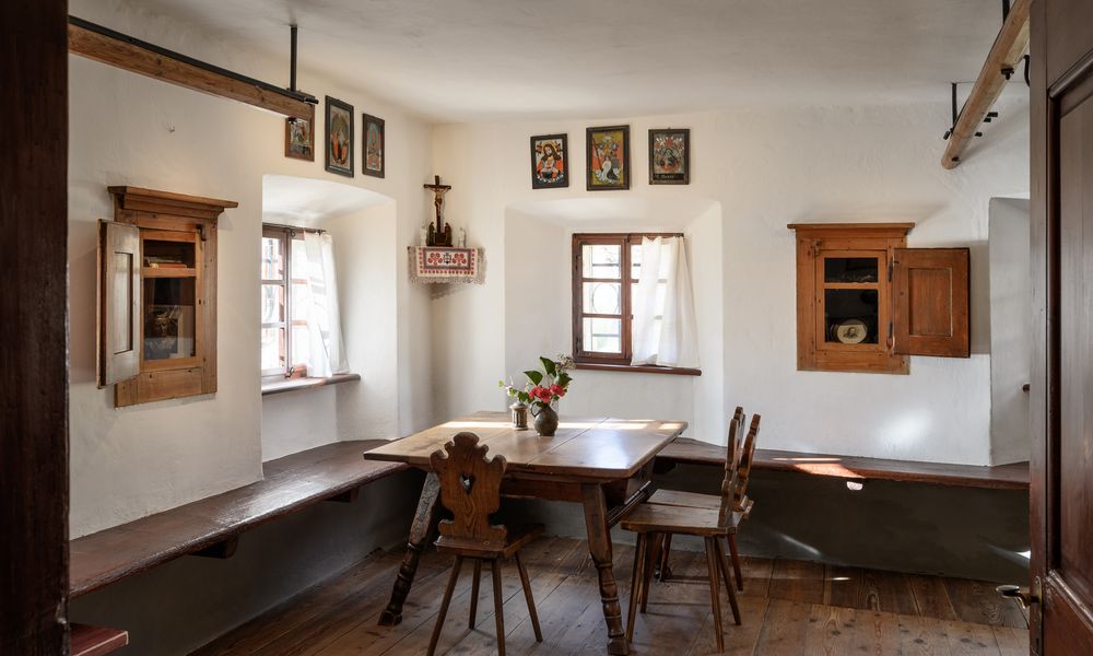 Miza in dva stola iz temnega lesa v kotu sobe v Prešernovi hiši, nad mizo sta na vsaki strani okni in leseni omarici v zidu. Na polički v kotu je križ, ob njem visijo nabožne podobe