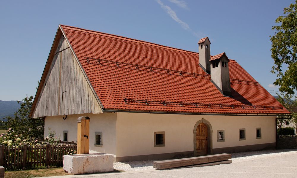 Prenovljena Prešernova hiša v Vrbi z dvema dimnikoma na rdeči strehi in majhnimi okni v pritličju.
