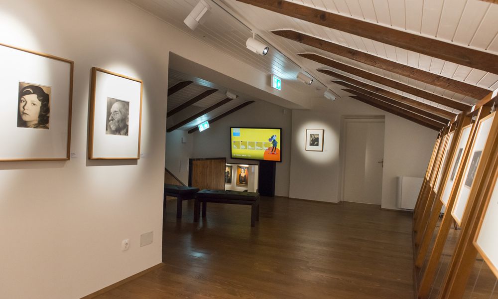 Podstrešni prostor galerije z razstavljenimi fotografijami in interaktivno tablo