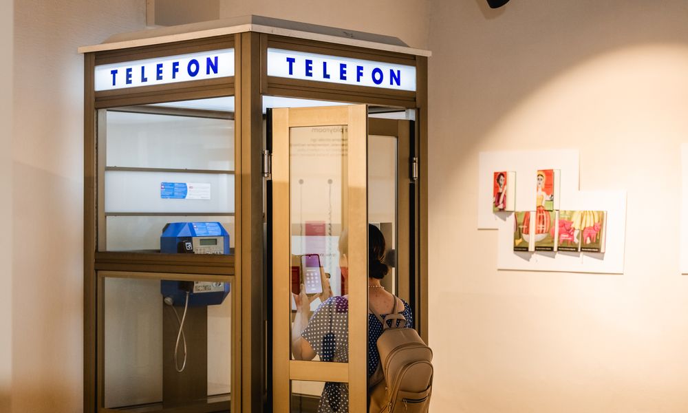 Ženska stoji v razstavljeni telefonski govorilnici na razstavi v Muzeju slovenskega jezika in knjige.