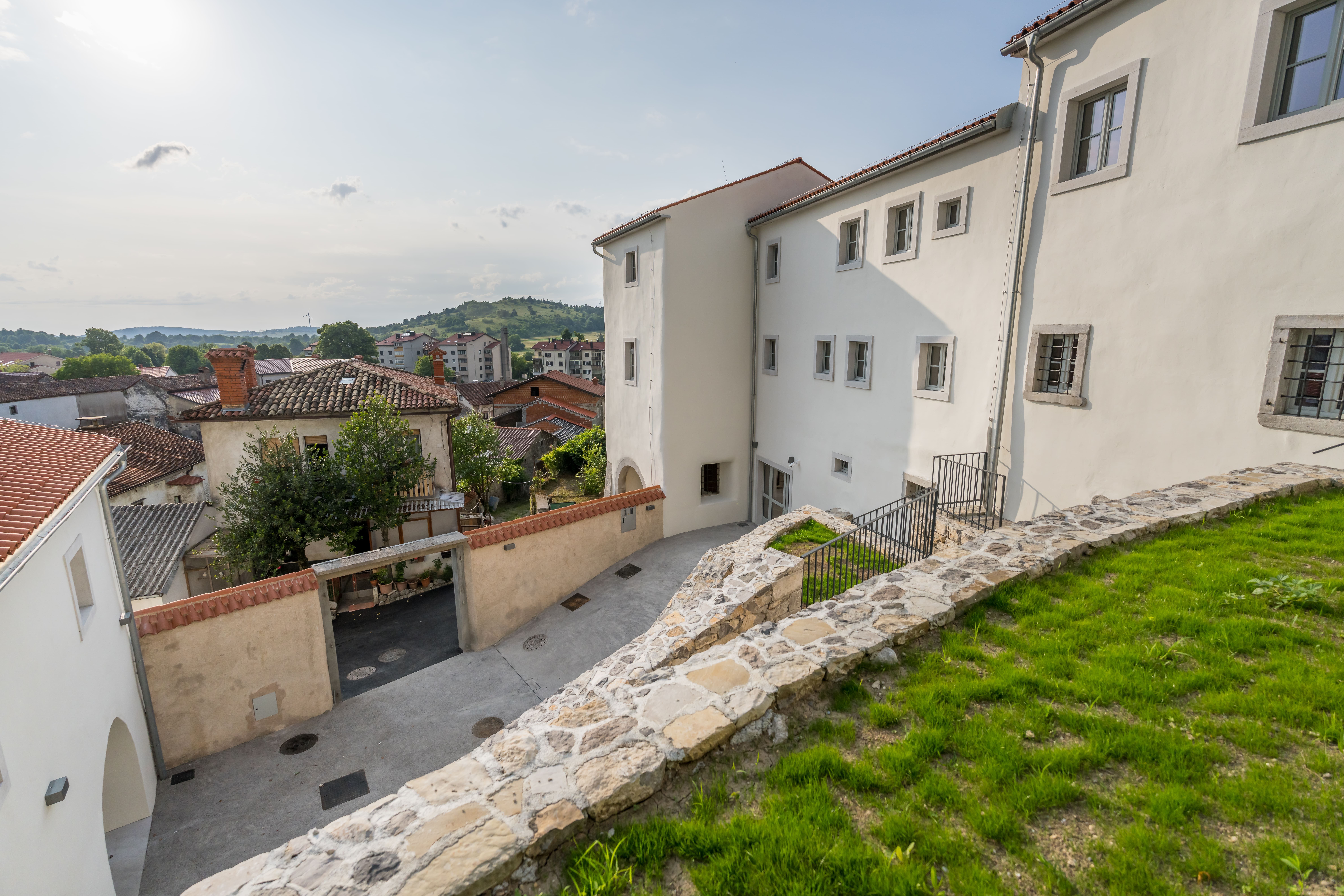 Zunanja podoba Muzeja prevozni&scaron;tva in tovorni&scaron;tva slikana iz travnatega dvori&scaron;ča, v ozadju pogled na Senožeče