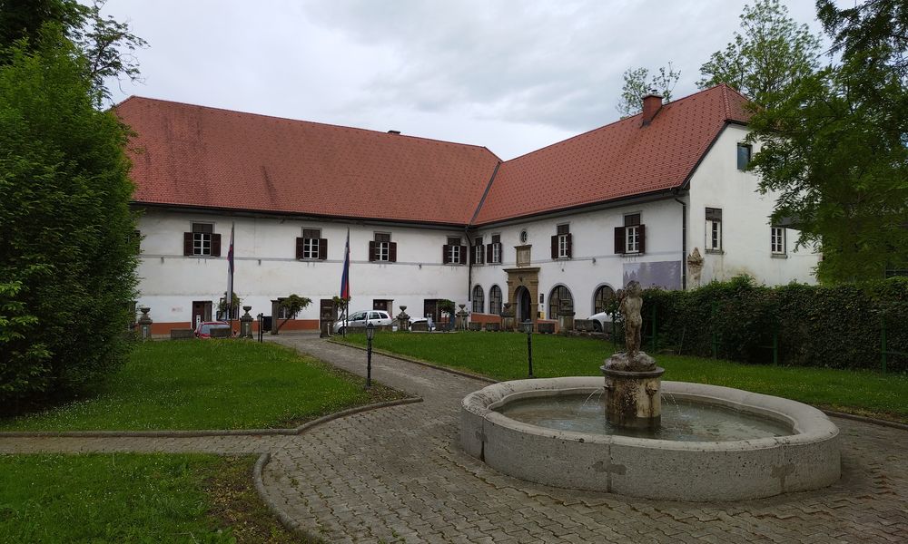 Zunanji pogled na dvorec Radlje po obnovi 2025, v ospredju vodnjak in manjši travnati park