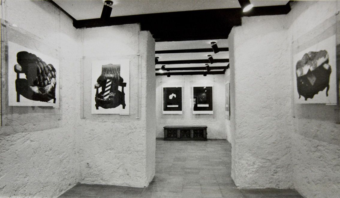 Črno-bela fotografija razstave v galeriji pred prenovo. Na belih stenah so umetni&scaron;ka dela.